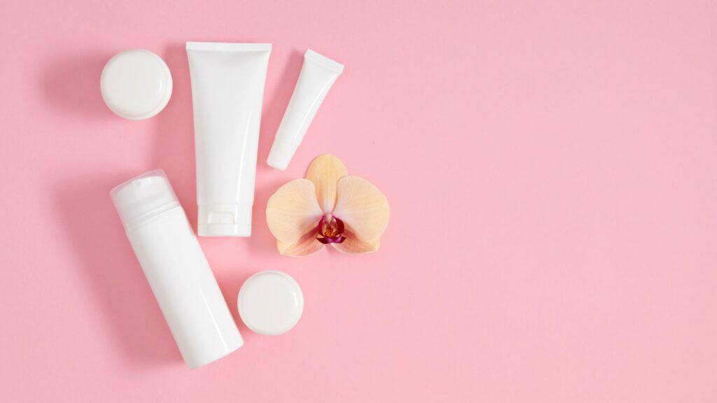 weisse kosmetikflaschen und cremetuben auf rosa hintergrund mit orchidee fuer verpackungsdesign
