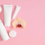 weisse kosmetikflaschen und cremetuben auf rosa hintergrund mit orchidee fuer verpackungsdesign