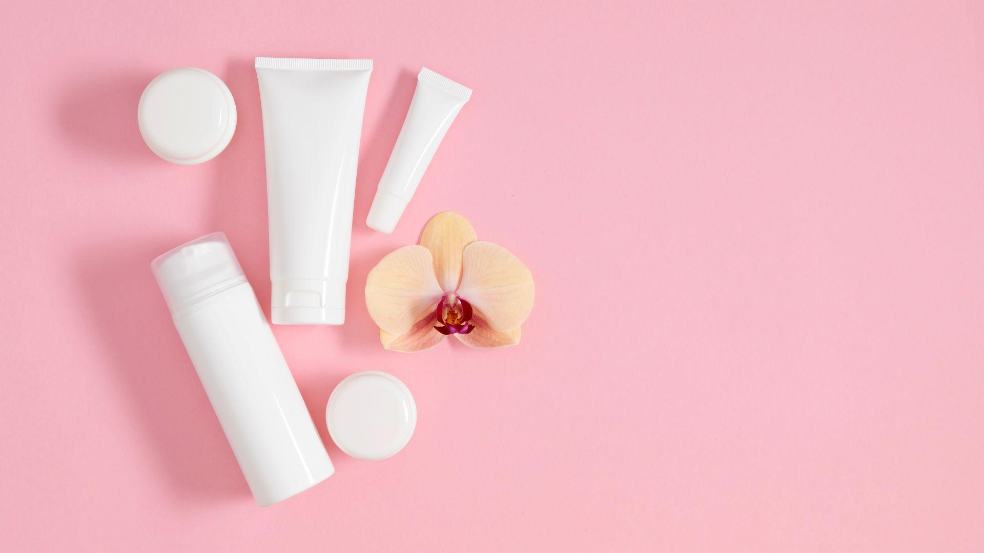 weisse kosmetikflaschen und cremetuben auf rosa hintergrund mit orchidee fuer verpackungsdesign
