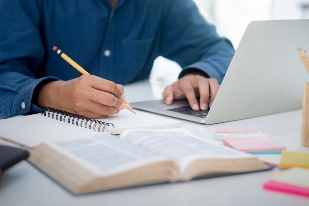 Schreiben und recherchieren mit Laptop und Buch | Ghostwriter Bachelorarbeit