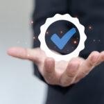 Hand haelt digitales Pruefsiegel mit blauem Haken als Symbol fuer gepruefte Sicherheit durch Sachverstaendiger Loeschanlagen